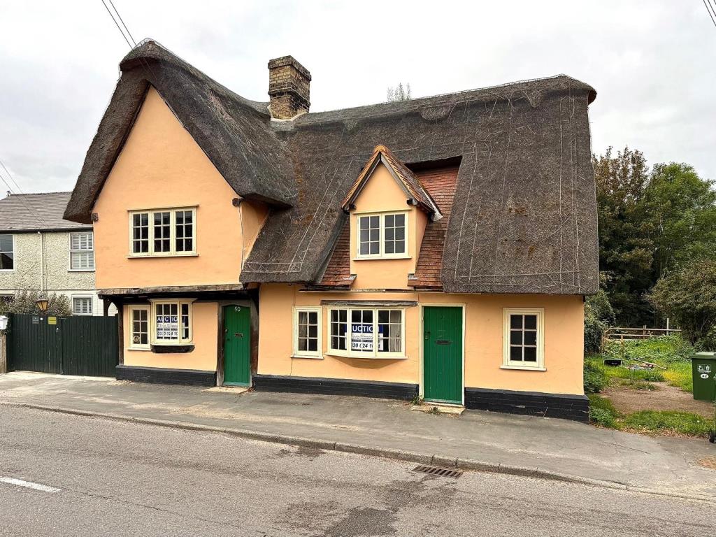 Lot: 115 - A PAIR OF THATCHED COTTAGES IN NEED OF IMPROVEMENT - Front shot showing view from road of thatched cottages